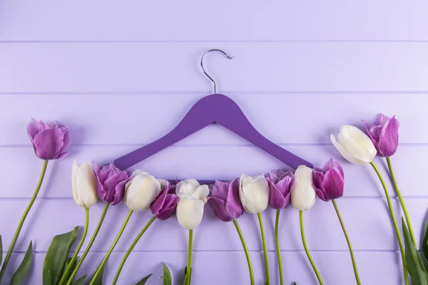 Hanger with purple and white tulips laid out along it on lilac wooden table. Concept of spring fashion.