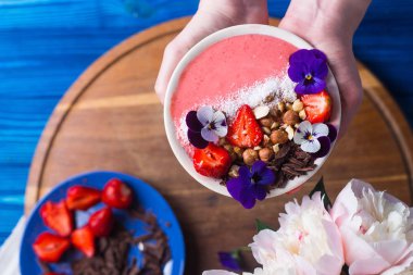 Portre genç erkek holding pembe yüzlü kase çilek, fındık, çikolata ile eller ve çiçeklerle, üstten görünüm dekore edilmiş.