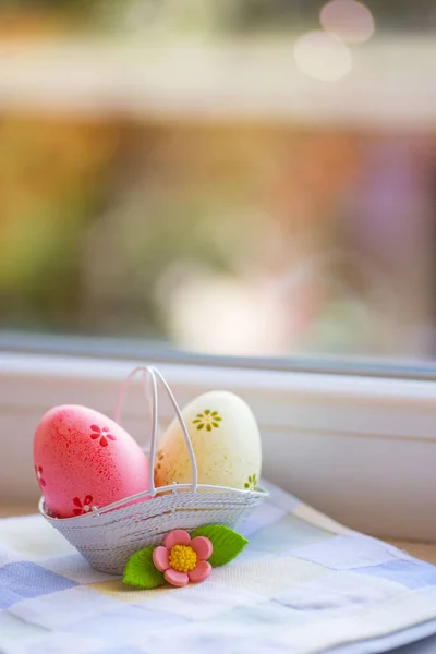 Coloridos huevos de Pascua rosados y amarillos en cesta con flores decorativas cerca de la ventana a la luz del día . — Foto de Stock