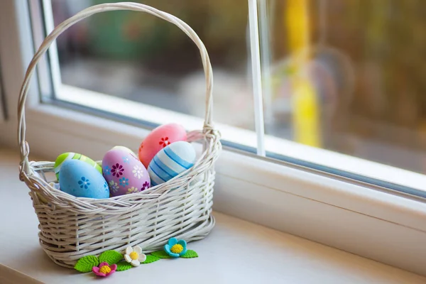 Varietà di uova di Pasqua colorate decorate in cesto di vimini con fiori primaverili vicino alla finestra alla luce del giorno . — Foto Stock