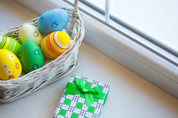 Scatola regalo verde e set di uova di Pasqua colorate decorate in cesto di vimini vicino alla finestra alla luce del giorno . — Foto Stock