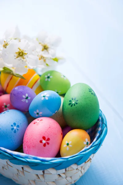 Vielfalt an verzierten bunten Ostereiern im Korb mit weißen Frühlingsblumen auf hellblauem Hintergrund — Stockfoto