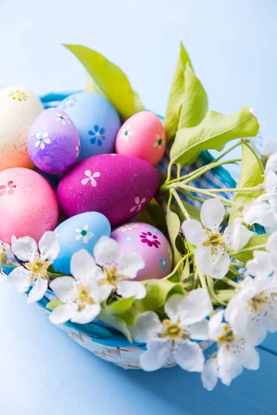 Nahaufnahme-Set dekorierter bunter Ostereier im Korb mit weißen Frühlingsblumen auf hellblauem Hintergrund — Stockfoto