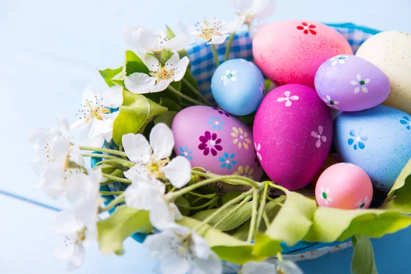 Closeup set of decorated colorful Easter eggs in basket with white spring flowers on light blue background — Stock Photo, Image