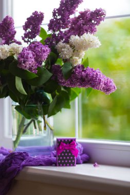 Mor hediye kutusu ve gün ışığında pencere yakınında cam vazo güzel leylak ihale buket.