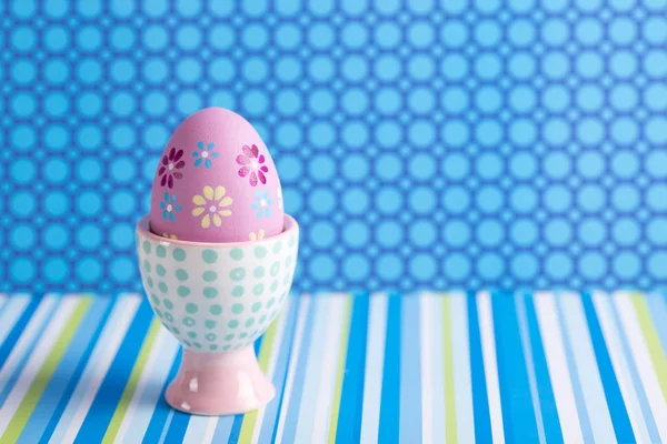 Primer plano colorido pintado huevo de Pascua en soporte de huevo moderno vibrante sobre fondo azul manchado y rayado . — Foto de Stock