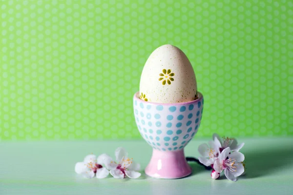 Primer plano colorido pintado huevo de Pascua en pie de huevo moderno vibrante rodeado de ramas de árbol de floración blanca sobre fondo verde . — Foto de Stock