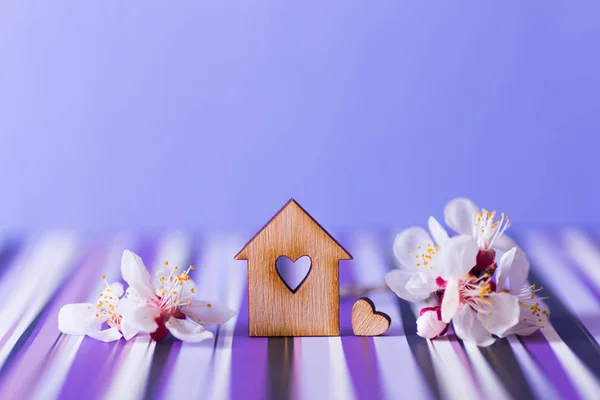 Nahaufnahme Holzhaus mit Loch in Herzform, umgeben von weiß blühenden Zweigen auf violettem Hintergrund. — Stockfoto