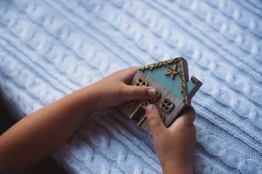 Çocukların elleri beyaz örgü arka planda dekoratif ahşap Noel evini tutuyor..