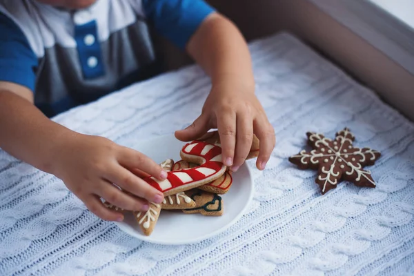 Niño tomando pan de jengibre de Navidad del plato en la mesa cerca de la ventana a la luz del día . — Foto de Stock