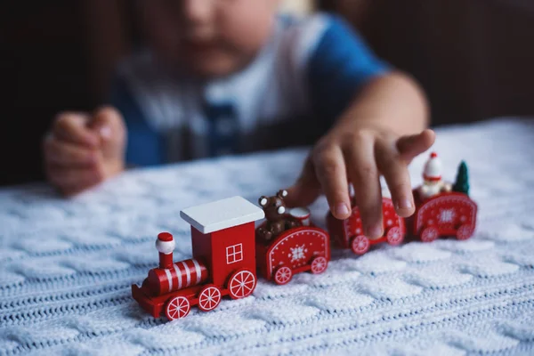 Niño jugando con juguete rojo tren de Navidad en punto blanco a cuadros a la luz del día . — Foto de Stock
