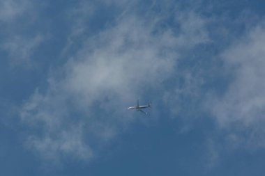 Mavi gökyüzünde, bulutların arasında uçan bir uçak.