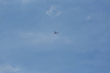 Mavi gökyüzünde, bulutların arasında uçan bir uçak.