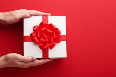 Hediye kutusu ile şerit kırmızı bir arka plan üzerinde tutan eller