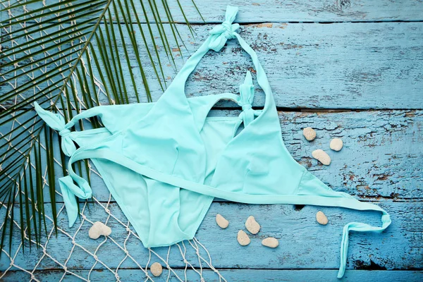 Swimsuit with green palm leaf and stones on blue wooden table