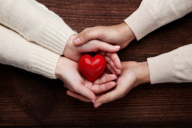 Kahverengi zemin üzerine kırmızı kalp tutan kadın ve erkek el