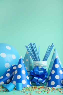 Birthday party caps, blowers and cups with paper straws on mint background clipart