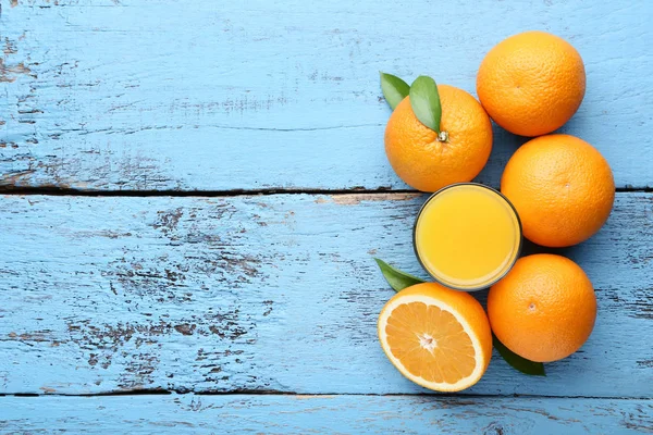 Oranges with green leaves and glass of juice on blue wooden table