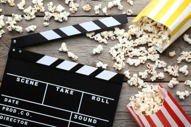 Clapper board with popcorn in paper bags on wooden table clipart