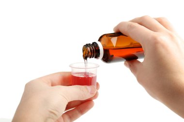 Erkek beyaz arka plan üzerinde plastik bardak ölçme içinde dökme tıbbi şurubu eller