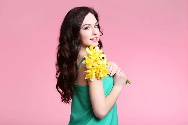 Beautiful young woman with narcissus flowers on pink background