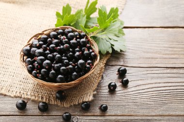 Sepeti ile siyah kuş üzümü yapraklar üzerinde gri ahşap masa