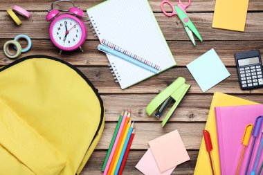 Kahverengi ahşap masa üzerinde sarı sırt çantası ile okul malzemeleri