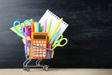 Okul malzemeleri karatahta arka planda alışveriş arabasında.