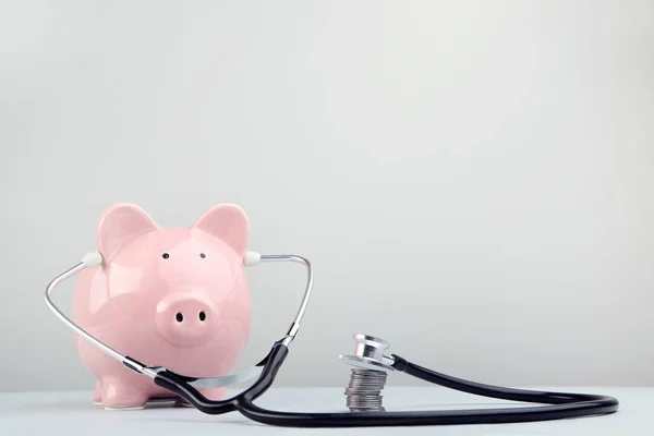 粉红色的小猪银行与听诊器和硬币的灰色背景 — 图库照片