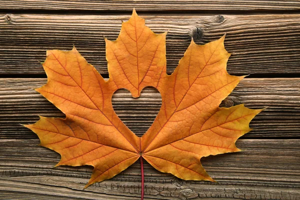 Dry maple leaf with heart on brown wooden table