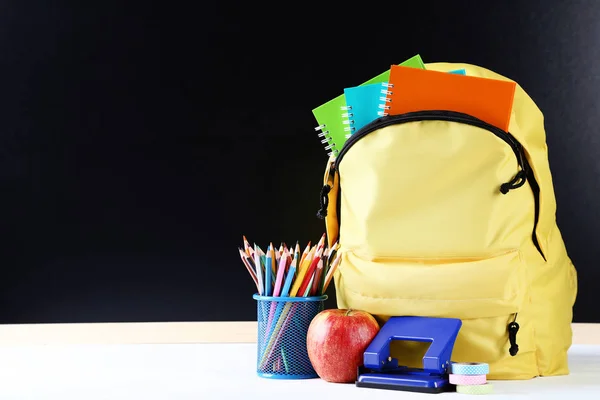 Yellow backpack with school supplies on black background