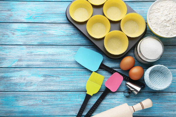 Пустые кексы с различными кухонными принадлежностями на деревянном столе
