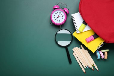 Yeşil arka plan üzerinde kırmızı sırt çantası ile okul malzemeleri