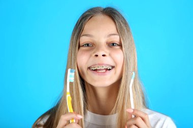 Diş diş telleri ve mavi arka plan üzerinde diş fırçası ile genç gülümseyen kız