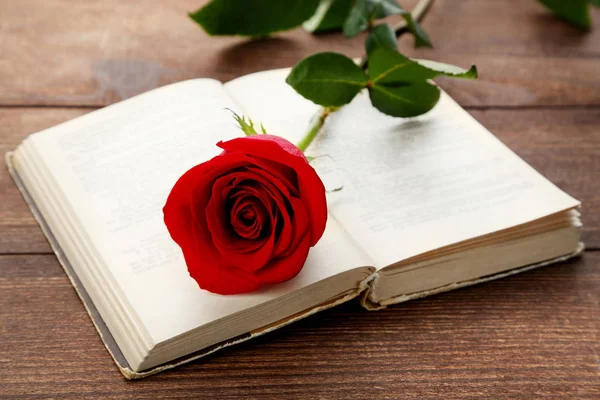 Red rose with book on brown wooden table