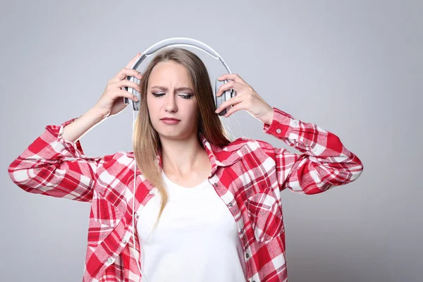 Young woman with headphones on grey background