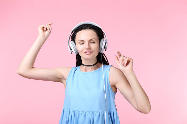 Young woman with headphones on pink background