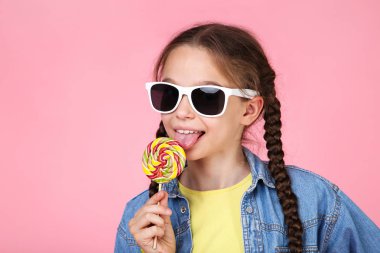 Lolipop ve pembe bir arka plan üzerinde güneş gözlüğü ile genç kız