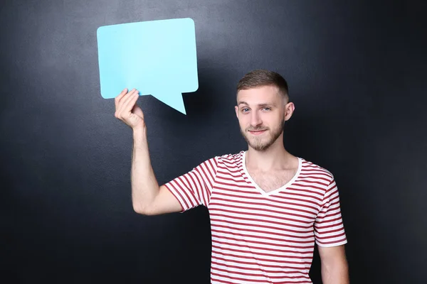 Young man holding speech bubble on blackboard background