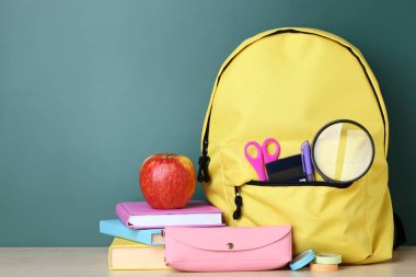Yeşil arka plan üzerinde sarı sırt çantası ile okul malzemeleri
