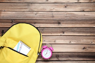 Sarı sırt çantası defter ve çalar saat ile kahverengi ahşap tablo