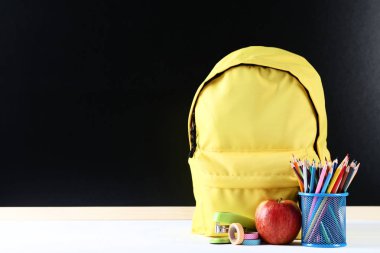 Siyah zemin üzerine sarı sırt çantası ile okul malzemeleri
