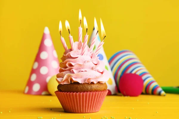 Cupcake with candles and paper caps on yellow background