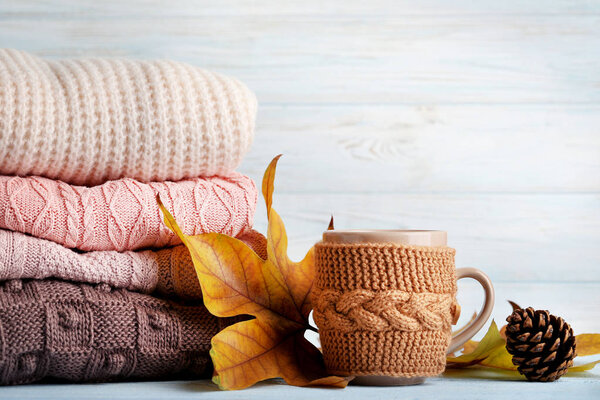 Stack of knitted sweaters with cup of tea and autumn leaves
