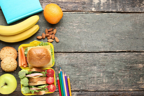 School lunch box with sandwich and vegetables on wooden table