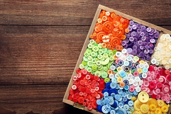 Colorful sewing buttons in basket on brown wooden table