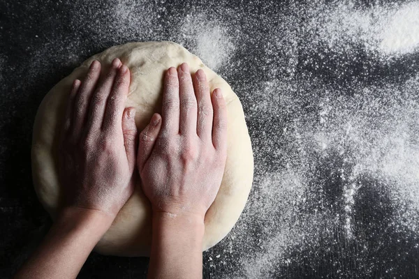 female hands knead dough on black wooden table