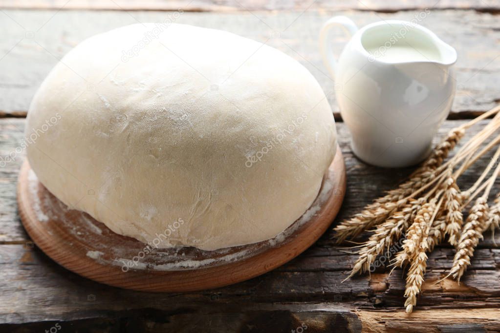 Raw dough with wheat ears and milk in jug on wooden table