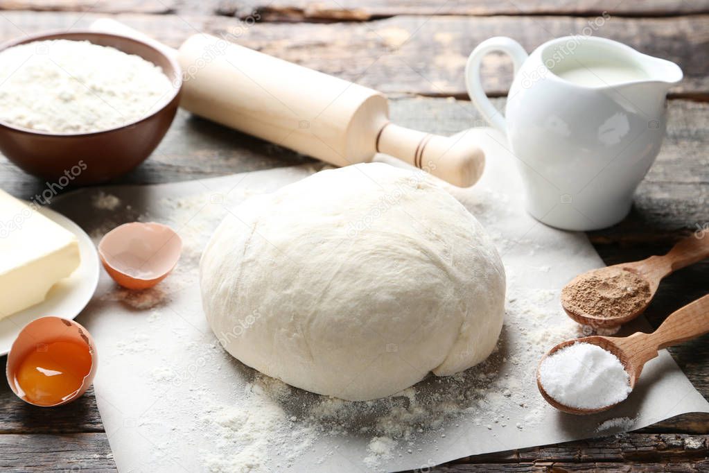 Raw dough with eggs, flour and milk in jug on wooden table