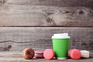 Kağıt bardak kahve ile gri ahşap masa üzerinde tatlı macaroons